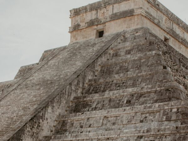 A woman in a floral sundress stands at the iconic Chichen Itza pyramid in Mexico.